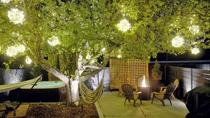 A tree with a hammock and chairs under it, a fire pit, and a wooden fence.