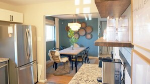 A modern kitchen with stainless steel appliances, a dining area with a wooden table and chairs, and a hanging light fixture.