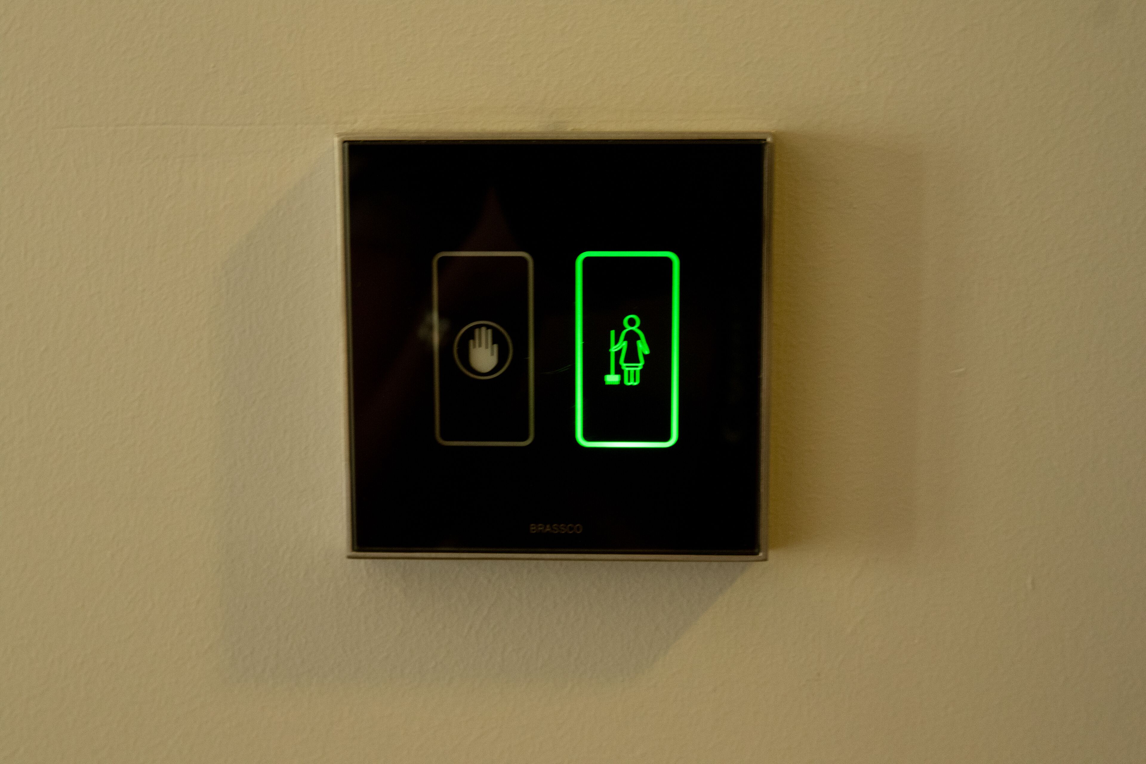 Een bedieningspaneel aan de muur met twee verlichte knoppen, waarvan één een handafbeelding heeft en de ander een staande persoon.