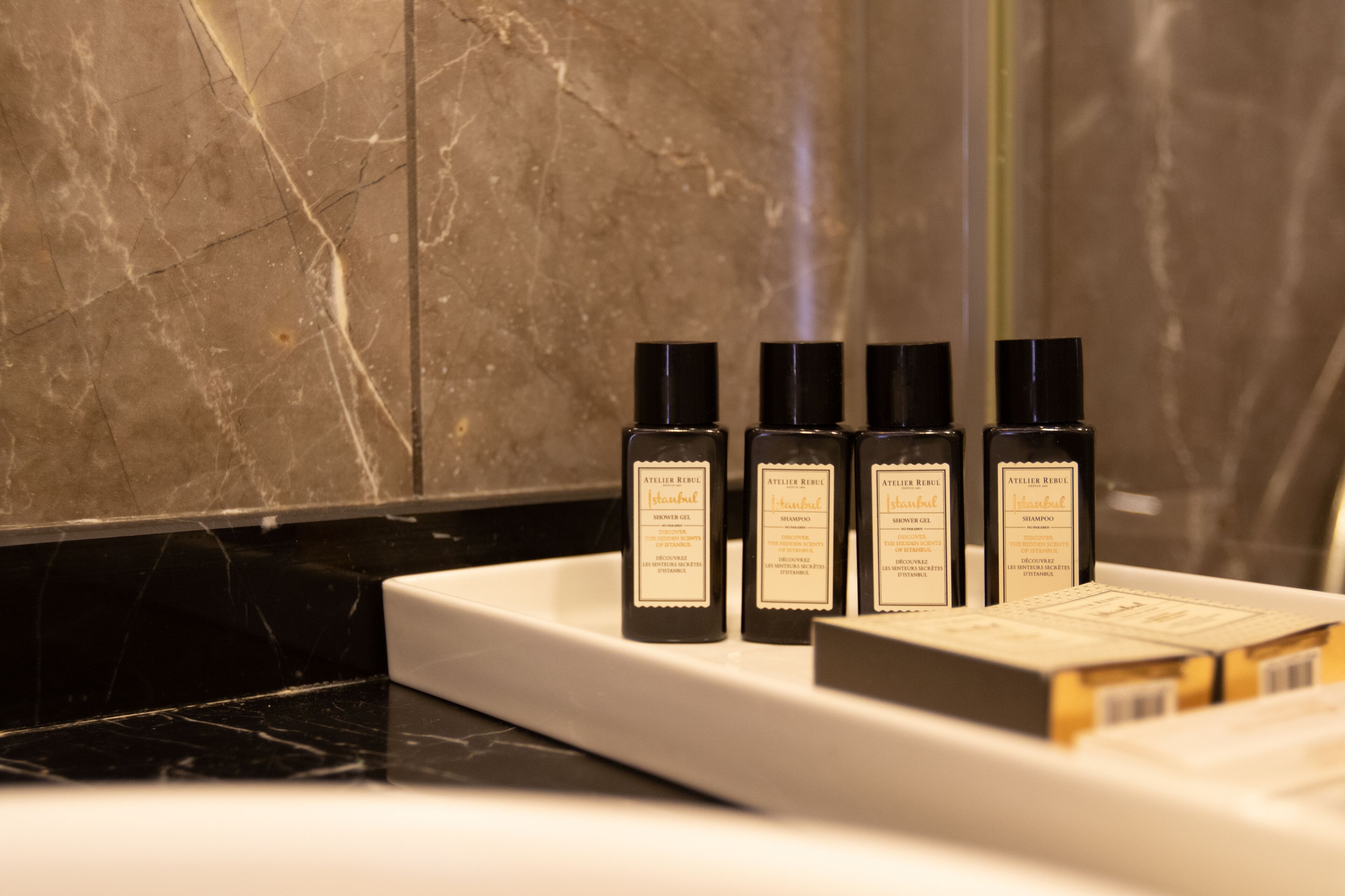 A bathroom with a marble countertop and four bottles of hair care products.