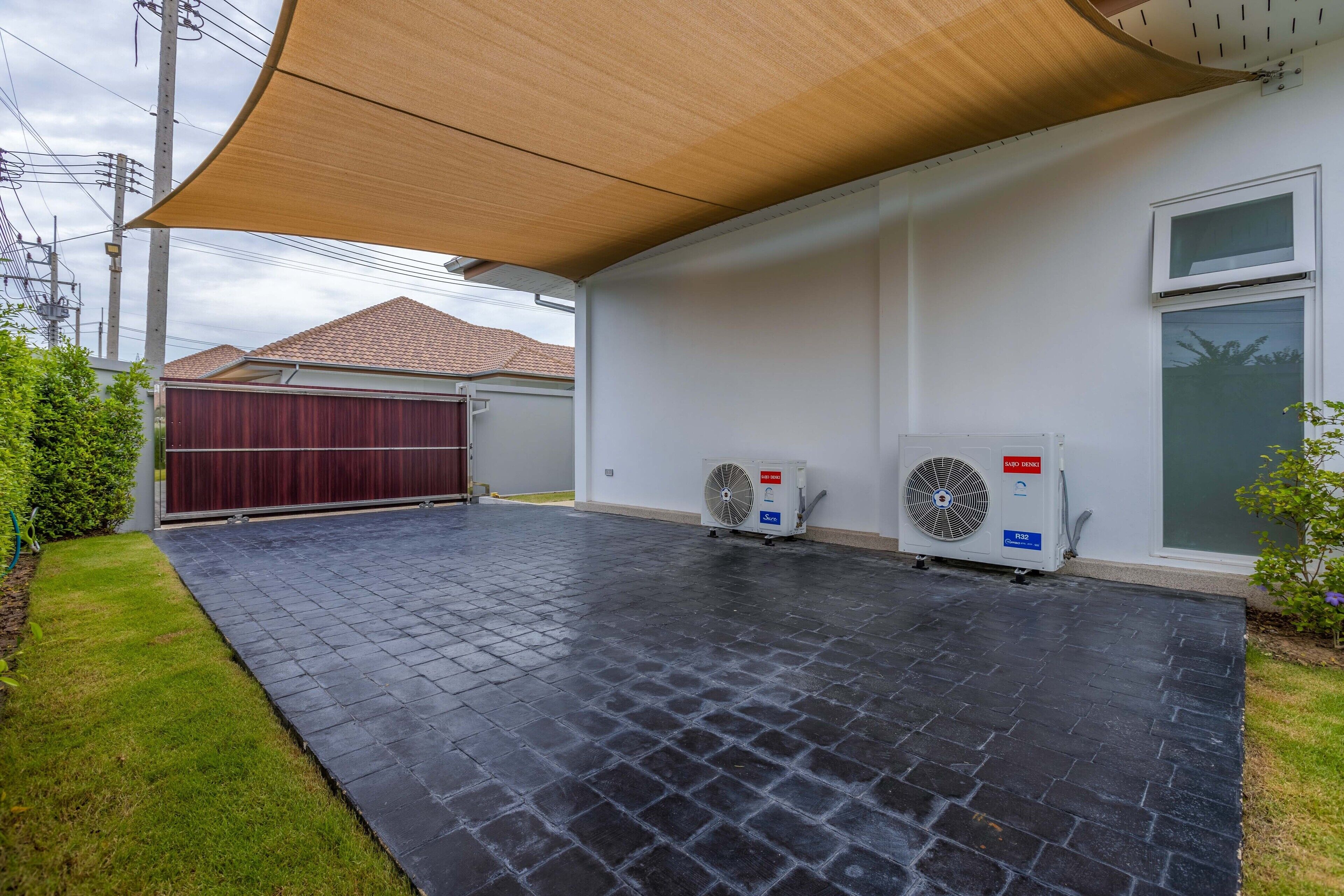 A covered outdoor area with a black tiled floor, two air conditioning units, and a red garage door.
