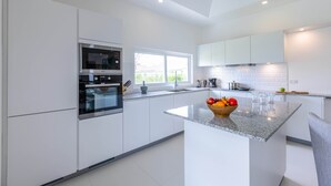 A modern kitchen with white cabinetry, a built-in oven, a large window, and a granite countertop with a fruit bowl. - Private 3 Bedroom Pool Villa MS22 (Hua Hin)