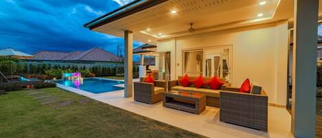 A modern outdoor living area with a pool, seating, and a covered patio.