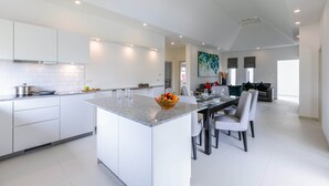 A modern kitchen with a central island, white cabinetry, and a dining area with a table and chairs. - Private 3 Bedroom Pool Villa MS22 (Hua Hin)
