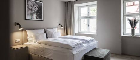 A modern bedroom with a bed, bedside tables, a window with curtains, and a framed picture on the wall.