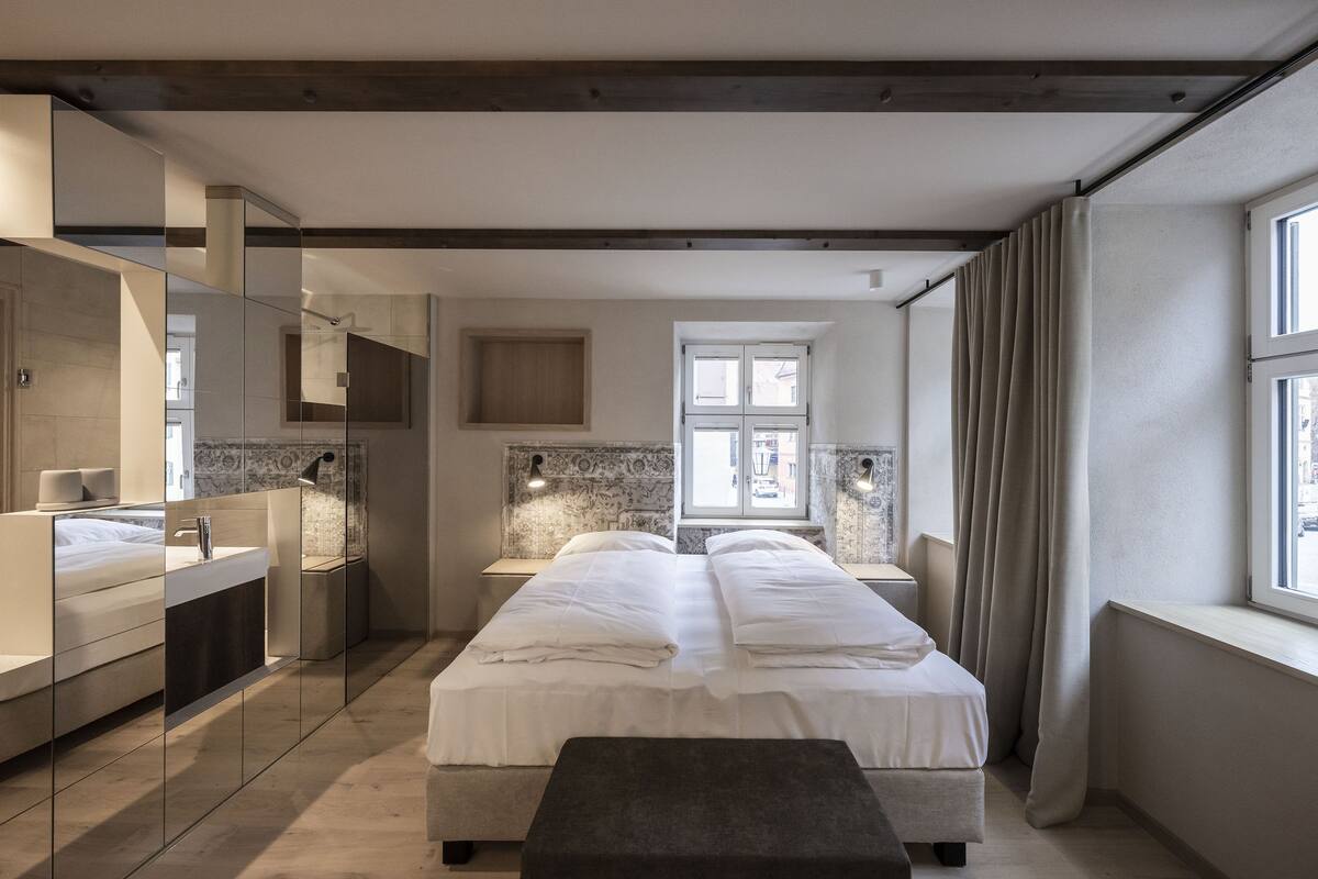 Ein modernes Schlafzimmer mit einem großen Bett, einem Nachttisch, einem Spiegel und einem Fenster mit Vorhängen.