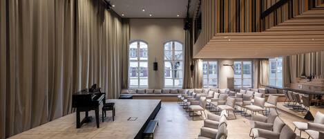 A spacious room with a piano, tiered seating, and large windows.