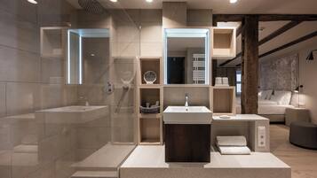 Un baño moderno con una bañera grande, un lavamanos y una zona de ducha. Hay un espejo sobre el lavamanos y un perchero a su lado.