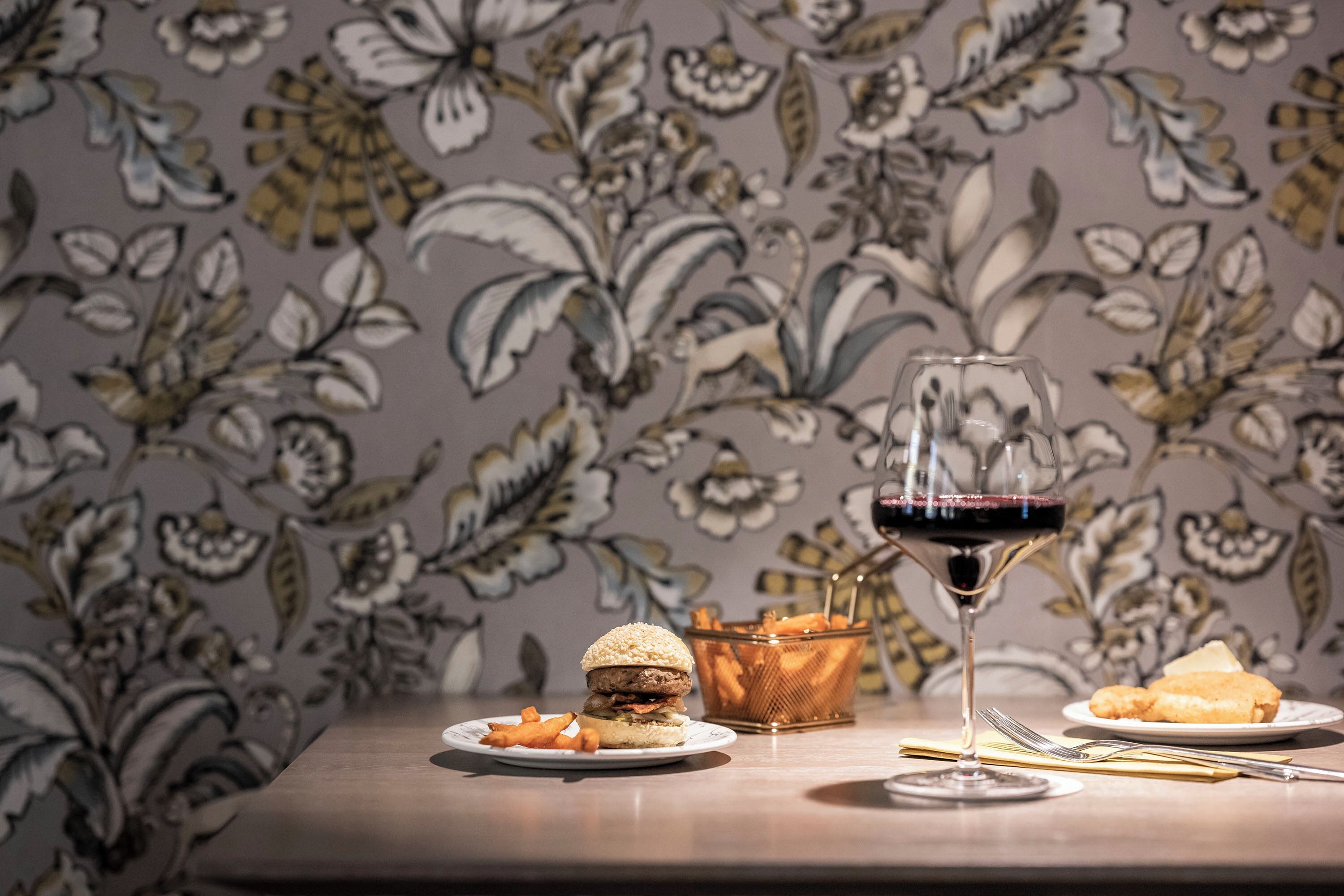 A dining table with a burger, fries, a glass of red wine, and a basket of chips.