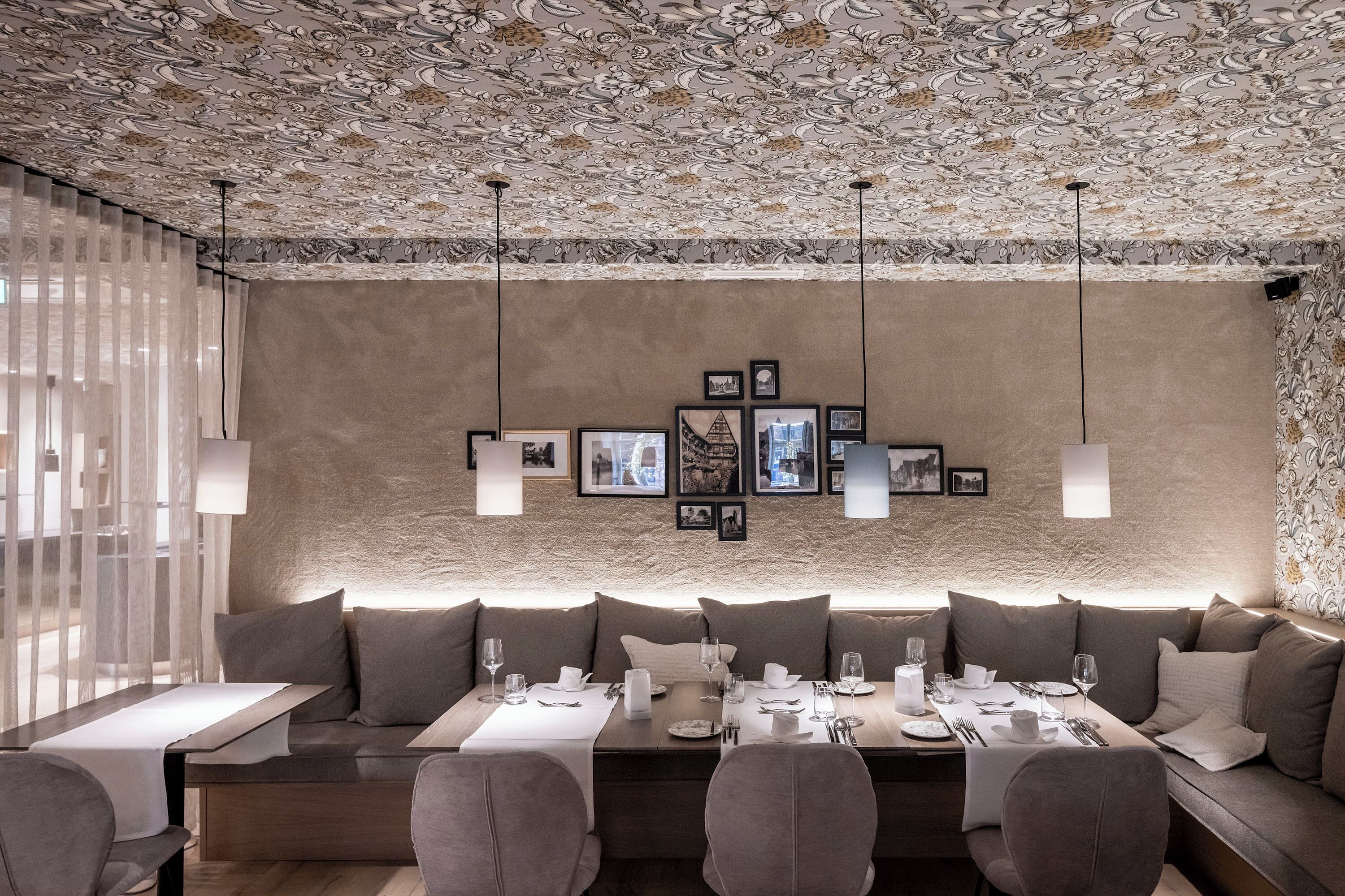A dining area with a long table set for a meal, cushioned seating, and a patterned ceiling.