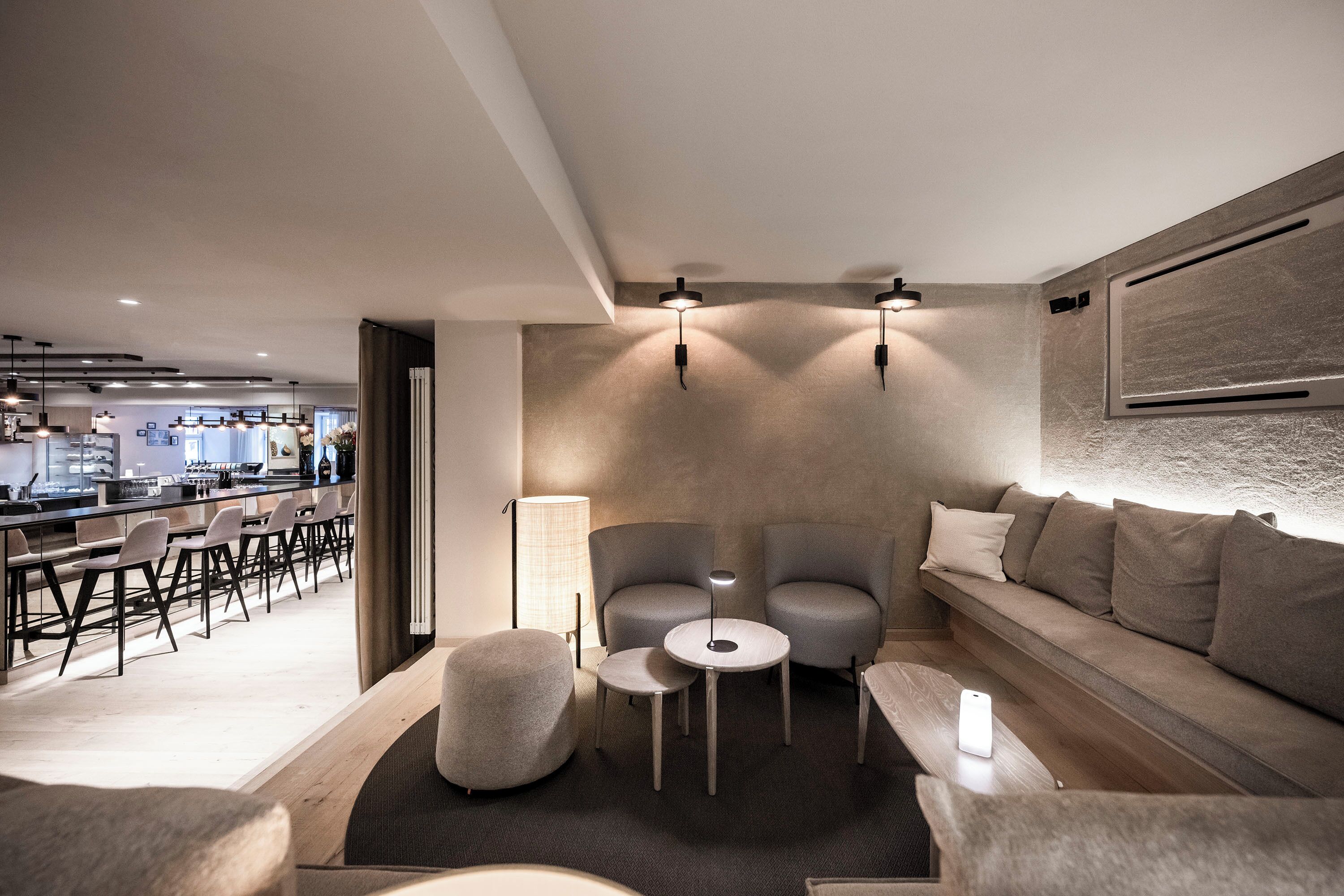 A modern living room with a sofa, two armchairs, a coffee table, and a dining area with chairs and a bar.