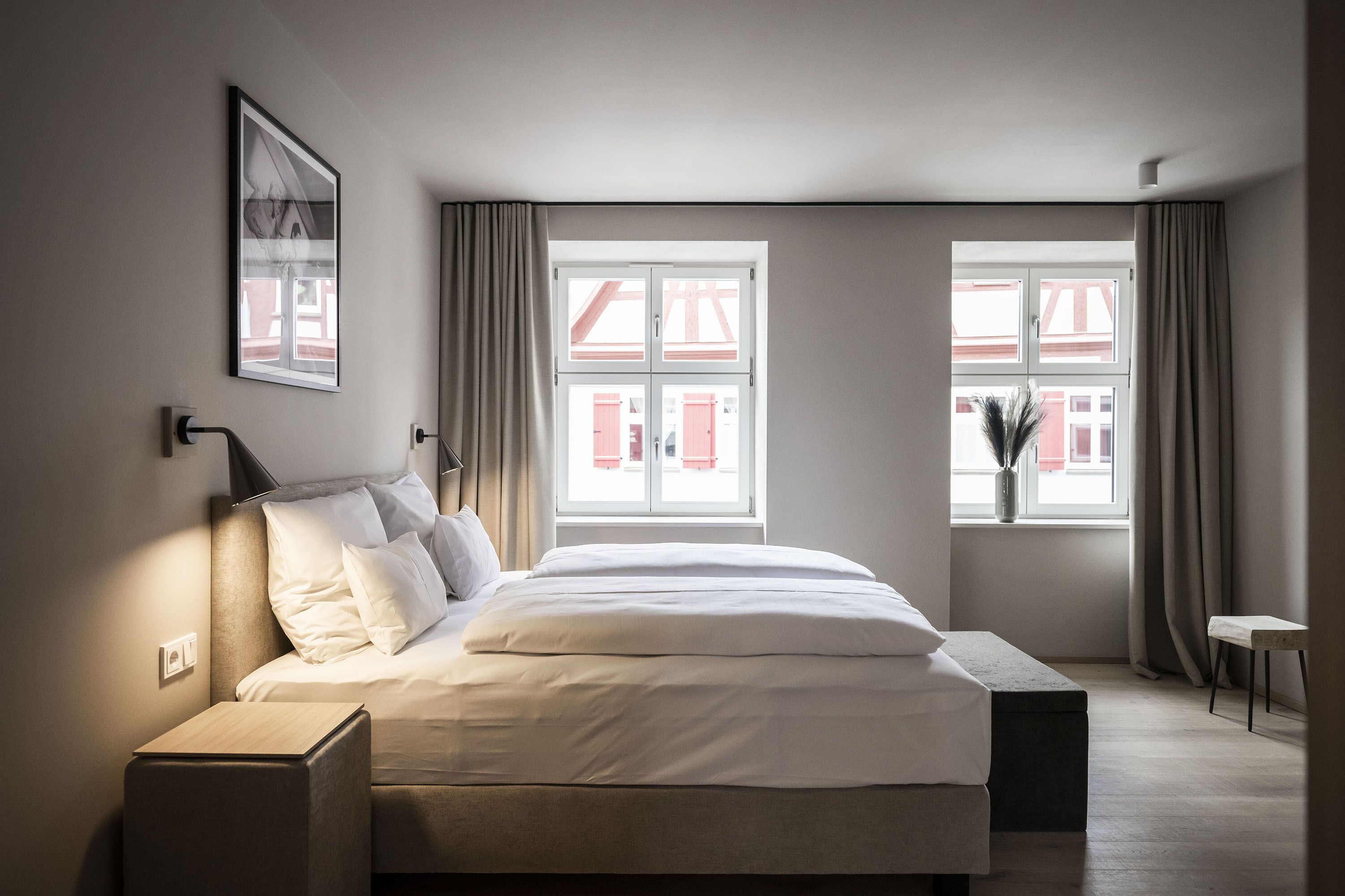 A modern bedroom with a large bed, two bedside tables, a bedside lamp, and a window with curtains.