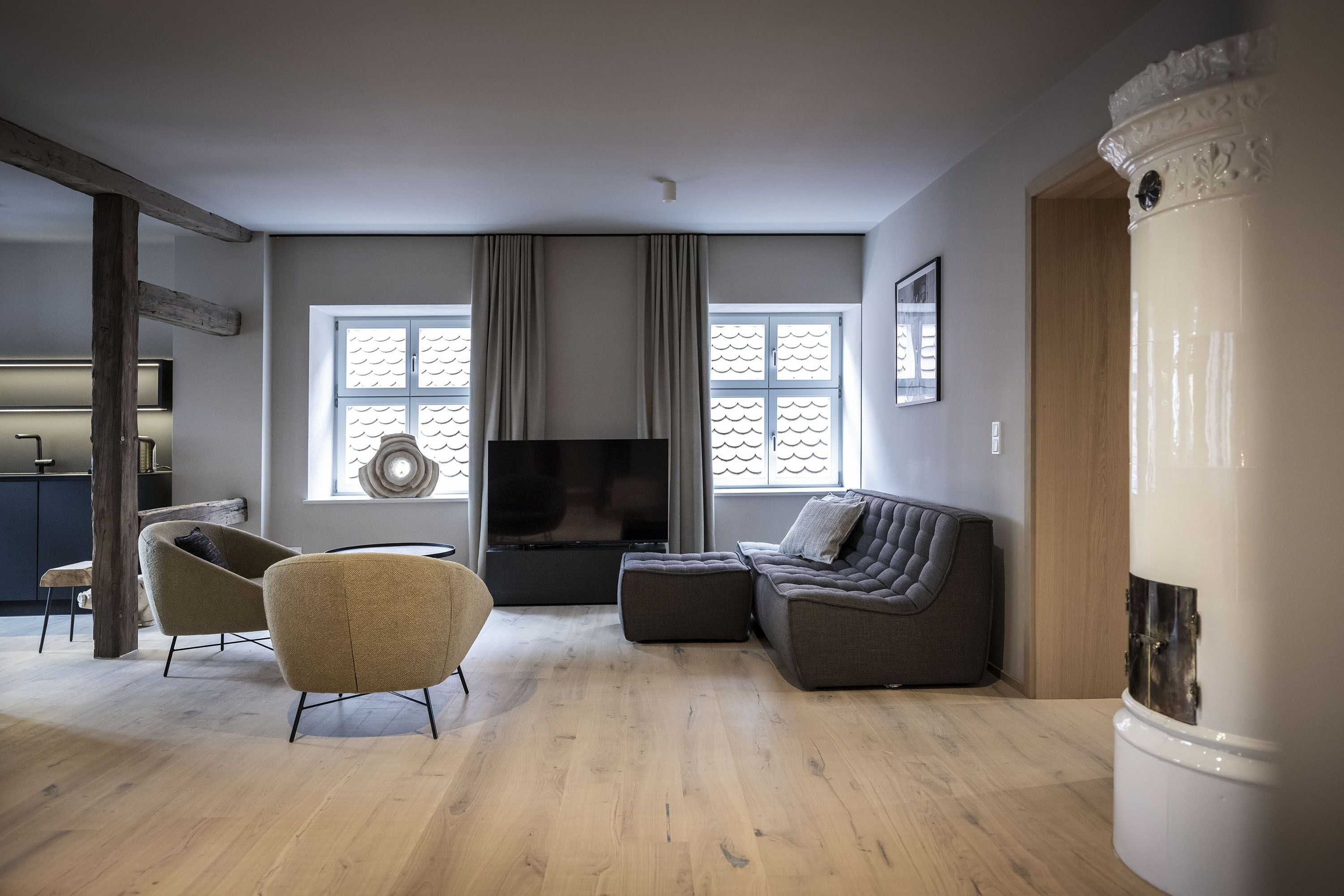 A modern living room with a sofa, armchair, and ottoman, a flat-screen TV, and a fireplace.