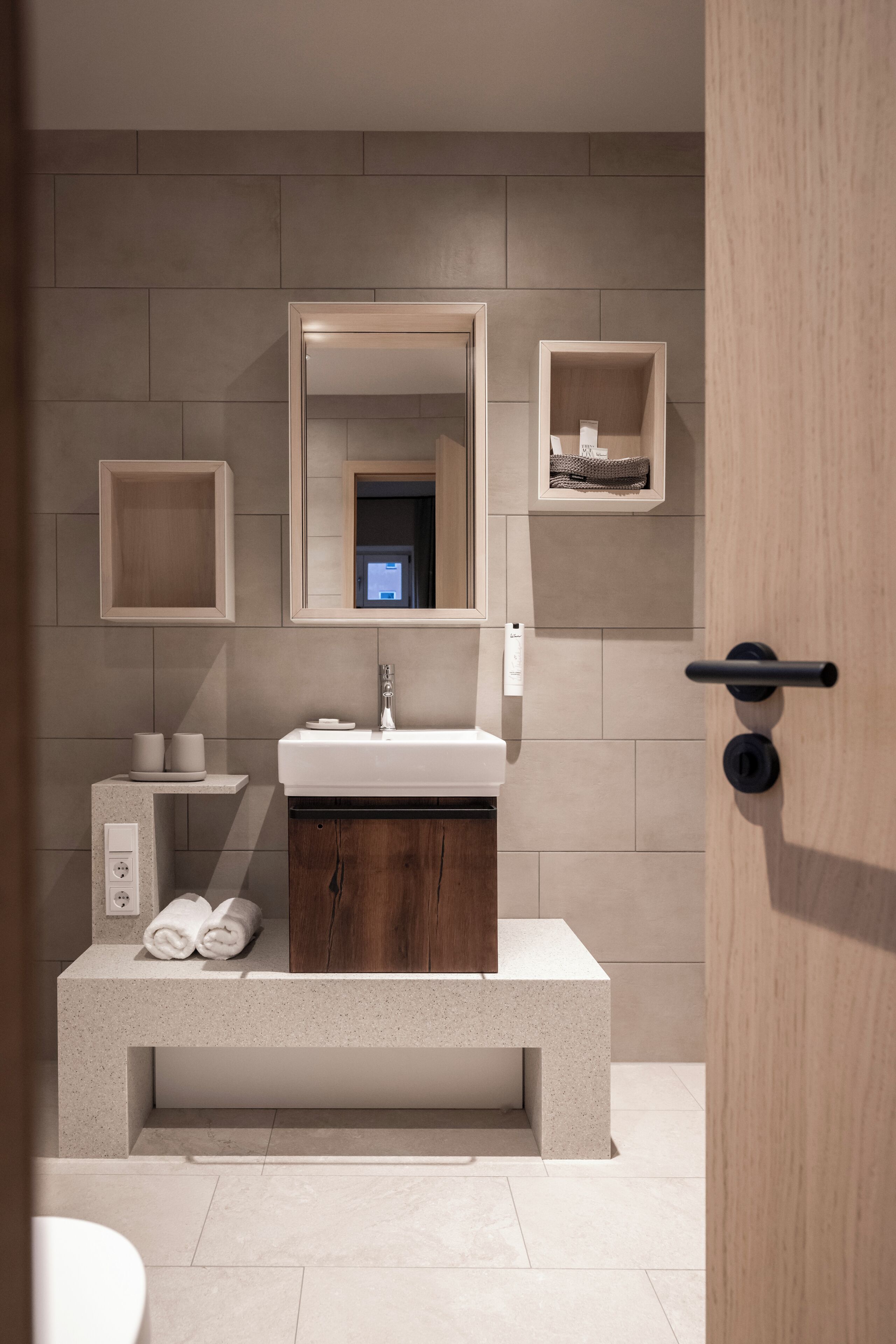 A modern bathroom with a large mirror, a white sink, and a wooden vanity.