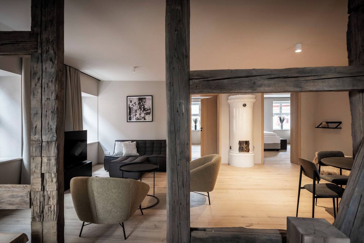 Ein modernes Wohnzimmer mit einer schwarzen Couch, beigen Sesseln und Holzboden.