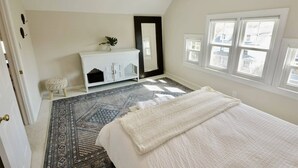A bedroom with a bed, a dresser, a mirror, a window, and a patterned rug.