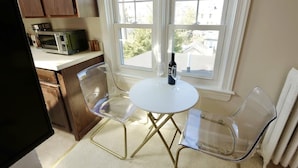 A kitchen with a microwave, two clear chairs, a small round table, and a bottle of wine.