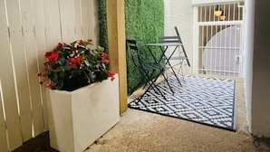 Um pátio com um tapete preto e branco, um vaso branco com flores vermelhas e uma mesa dobrável preta.