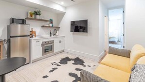 Um espaço compacto com cozinha compacta, televisão de tela plana, sofá e tapete de couro.