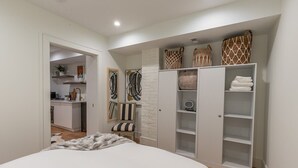 A bedroom with a bed, a wardrobe, a small seating area, and a kitchenette in the background.