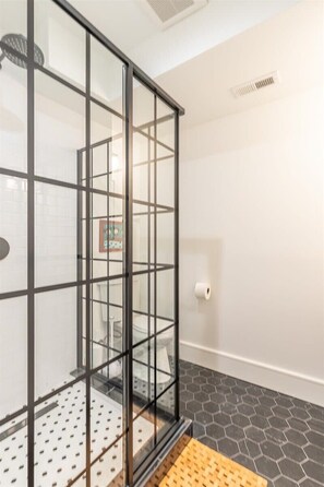 A modern bathroom with a glass shower enclosure, a white tiled wall, and a hexagonal patterned floor. - Delightful Apt in the Heart of Dupont! (Washington)