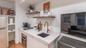 A modern kitchen with white cabinetry, a built-in oven, a gas stove, a sink with a gold faucet, and a large flat-screen TV.