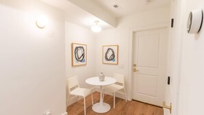 A room with a white door, two framed abstract paintings, a round white table with chairs, and a light fixture on the ceiling.