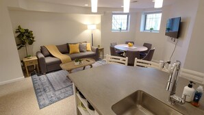 Et moderne køkken med indbygget vask, spiseområde med et rundt bord, og en stue med sofa og lampe.