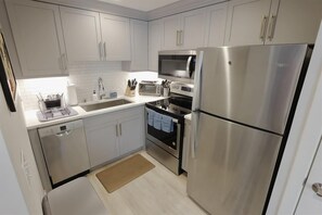 Une cuisine moderne avec des meubles blancs, des appareils en acier inoxydable, un lave-vaisselle et un four à micro-ondes.