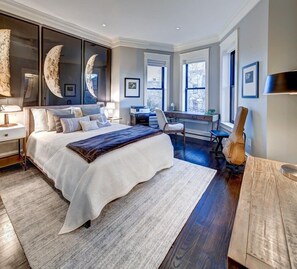 A modern bedroom with a large bed, a desk, and a guitar.