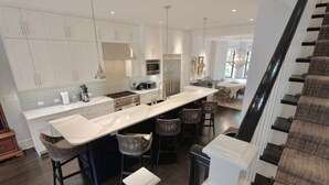 A modern kitchen with white cabinetry, a long island counter, and a dining area with a round table and bar stools. - Luxurious Mansion in Logan Circle Private Parking (Washington)