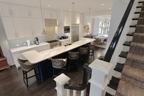 A modern kitchen with white cabinetry, a central island with bar stools, and a staircase leading to an upper level.