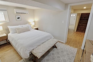 A bedroom with a bed, bedside tables, a rug, and a staircase leading to another room.