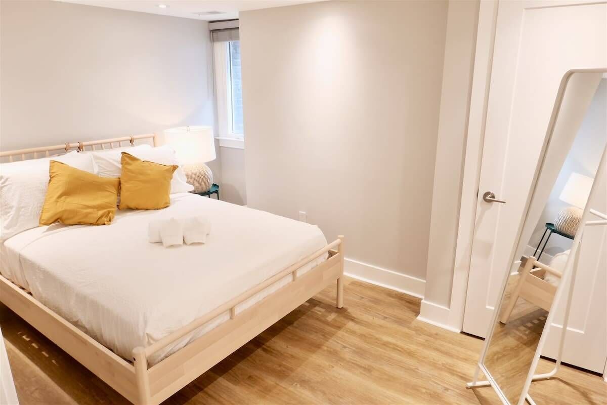 Un dormitorio con una cama de madera, una mesita de noche con lámpara, un espejo y una ventana.