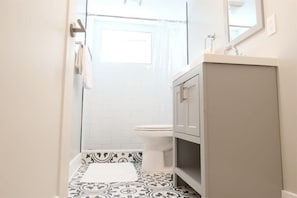 Ein schmales Badezimmer mit Toilette, Waschbecken mit Spiegel und Fliesenboden mit Muster.
