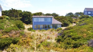 A two-story house with a sloped roof and large windows, surrounded by dense vegetation and hills. - New Listing! Cozy beachfront getaway with amazing views and miles of sandy beaches (Florence)