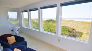 A room with a large window overlooking a beach, a white chair, and a blue sofa with cushions. - New Listing! Cozy beachfront getaway with amazing views and miles of sandy beaches (Florence)