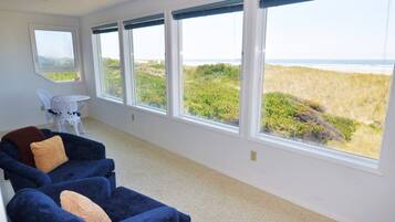A room with a large window overlooking a beach, a white chair, and a blue sofa with cushions.
