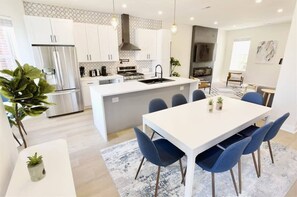 A modern kitchen with white cabinets, a central island, and blue chairs.
