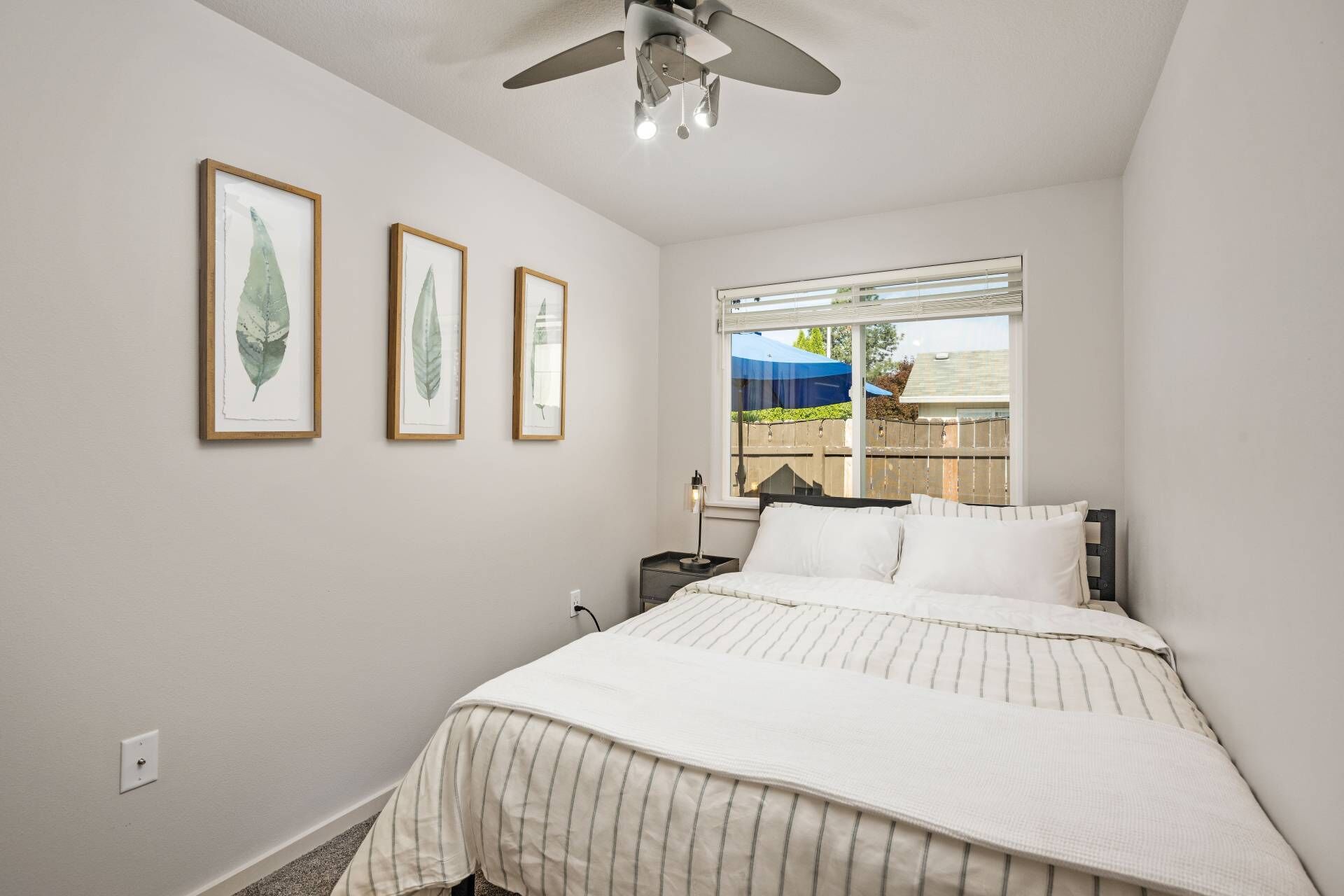 Ein Schlafzimmer mit einem Bett, einem Deckenventilator und drei gerahmten Pflanzenbildern an der Wand.