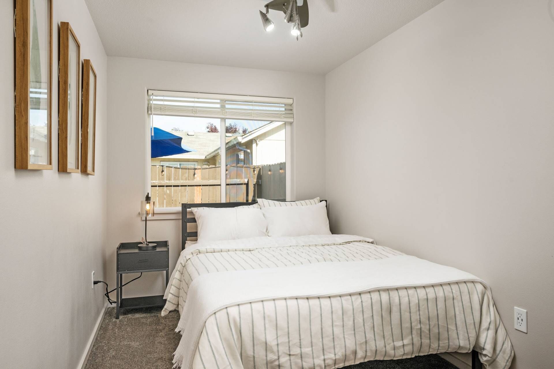 A bedroom with a bed, a nightstand, a lamp, and a window with blinds.