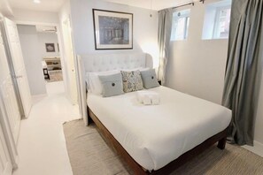 Un dormitorio con una cama grande, un cabecero, un cuadro en la pared y vistas al exterior a través de una ventana.