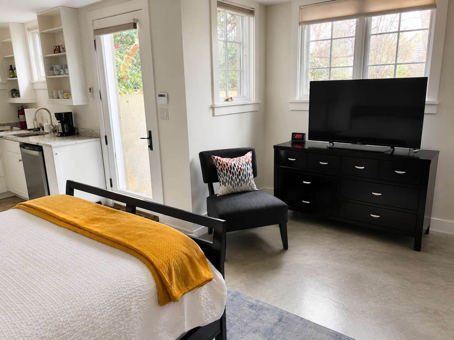 Une chambre à coucher comprenant un lit, un téléviseur, une chaise, une commode et un coin cuisine avec une machine à café.