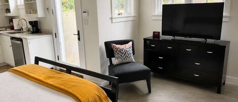 Une chambre à coucher comprenant un lit, un téléviseur, une chaise, une commode et un coin cuisine avec une machine à café.