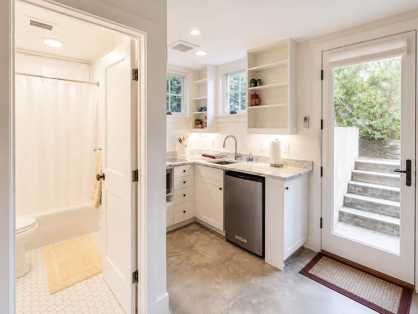 A modern kitchen with white cabinetry, a dishwasher, and a window overlooking greenery.