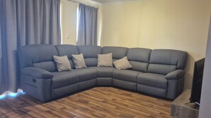 Een modulaire bank met vier kussens in een woonkamer met houten vloer en een televisie op een dressoir.