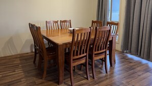 Een eetgedeelte met een houten tafel en stoelen, een airconditioner en een raam met gordijnen.