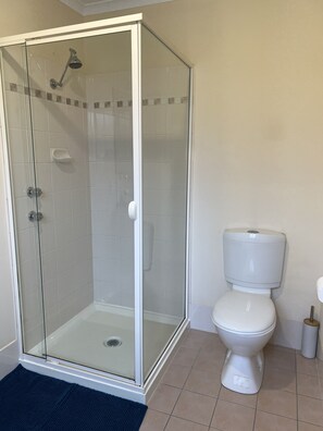 Une salle de bain avec une douche à parois de verre, des toilettes blanches et un tapis de bain bleu.