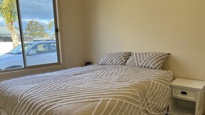 Een slaapkamer met een bed, nachtkastje en raam.