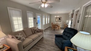A living room with a beige sofa, a blue armchair, a wooden coffee table, and a ceiling fan.